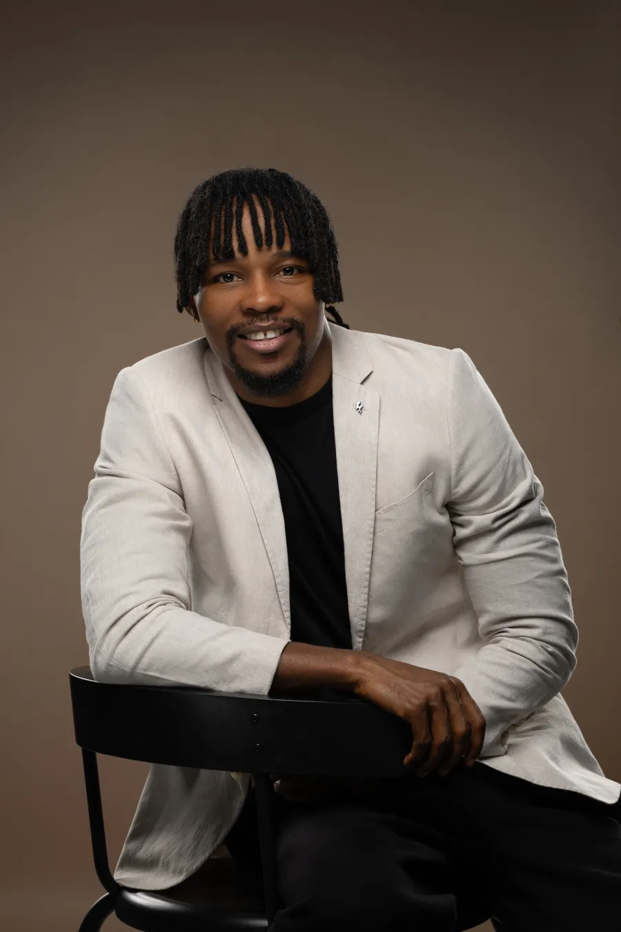 Kenny smiling, seated with his arms resting on a chair